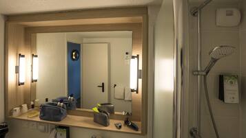 A bathroom with a large mirror, a shower, and a sink.