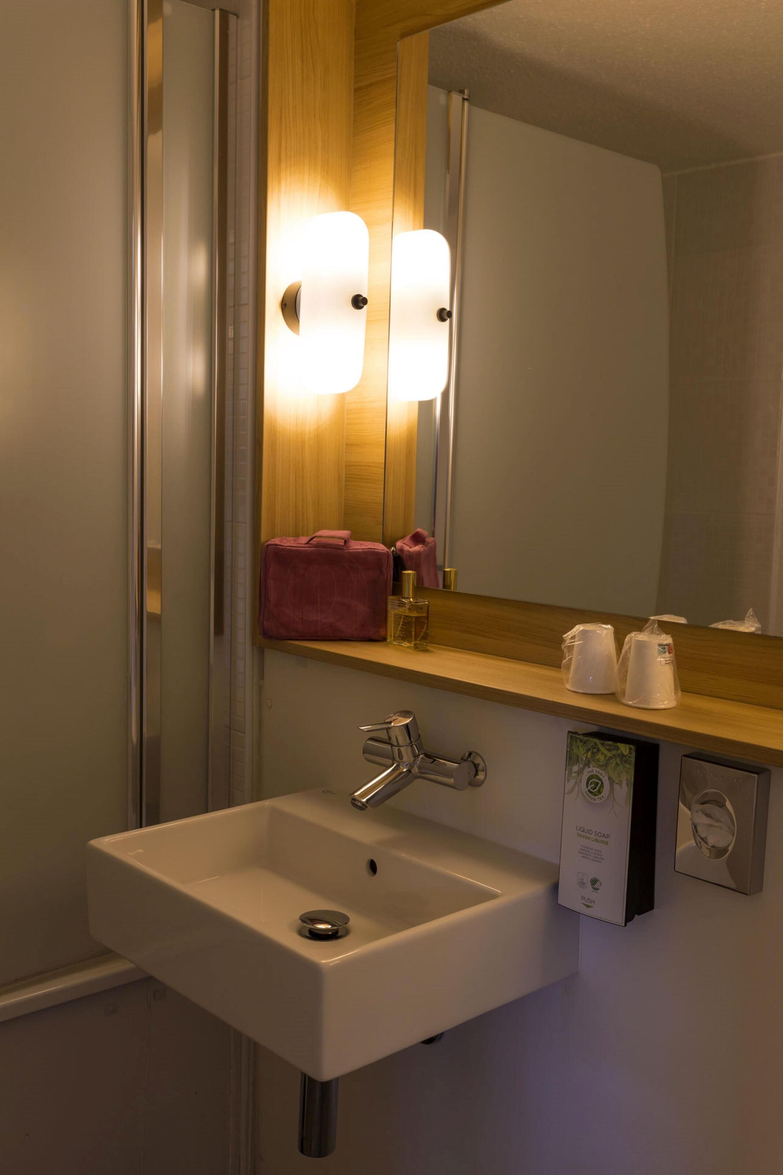 Un bagno con un lavandino bianco, uno specchio e uno scaffale in legno con articoli da toilette.