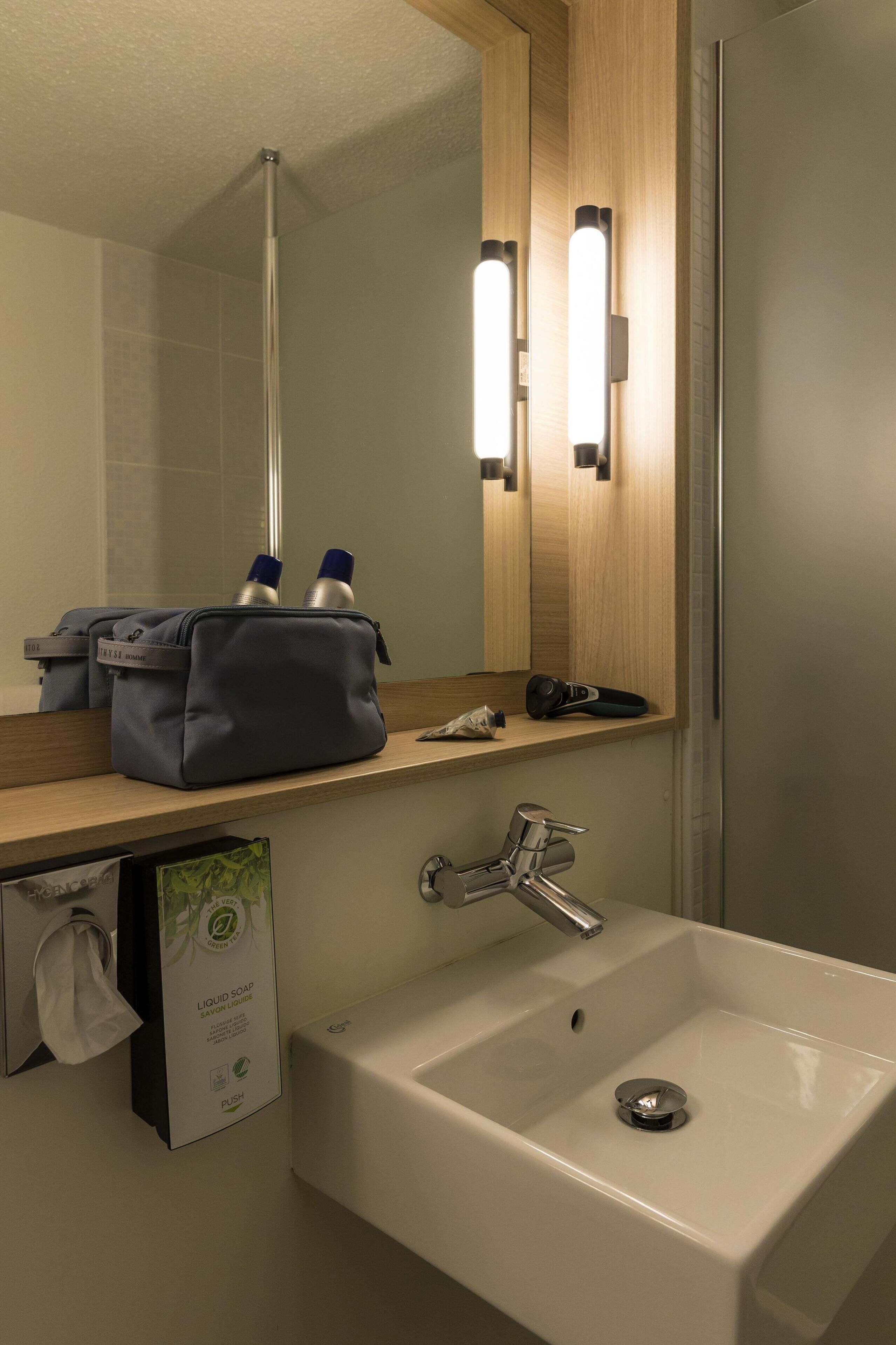 A hotel bathroom with a white sink, a mirror, and a towel dispenser.