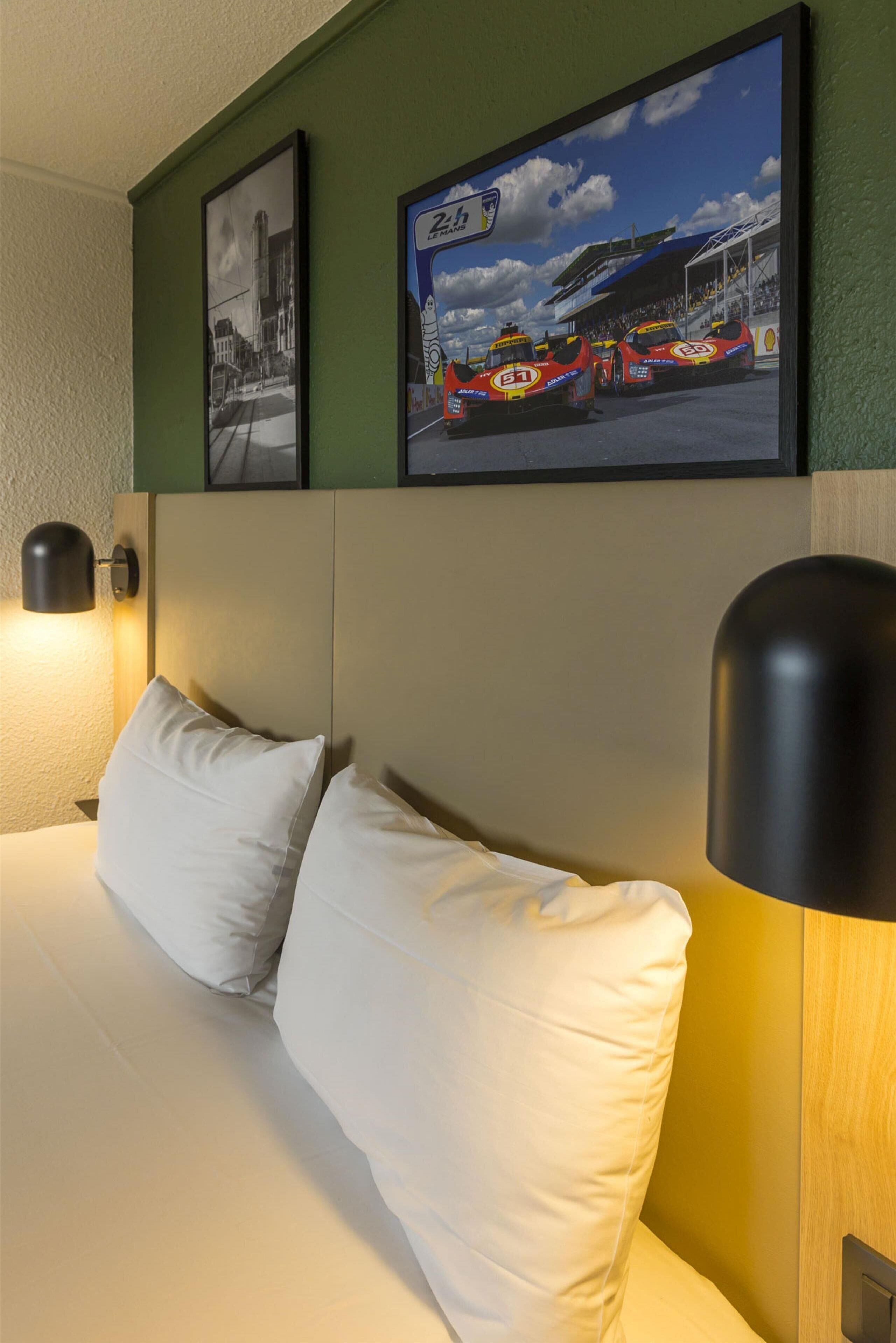 Quarto de hotel com cama, duas almofadas, cabeceira e duas luminárias fixadas na parede.