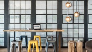 A modern bar area with a wooden table, multiple stools, and hanging pendant lights. - Campanile Katowice (Katowice)