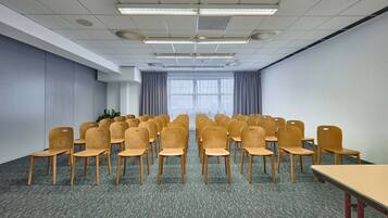 Un salón de conferencias con hileras de sillas de madera, piso alfombrado y ventanas amplias con cortinas.