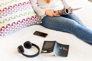 A person sitting on a bed with a book, a smartphone, and headphones. - Campanile Katowice (Katowice)