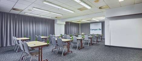 A conference room with tables, chairs, and a projection screen.