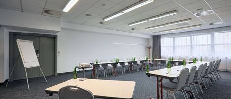 Une salle de conférence équipée d’une longue table, de chaises, d’un projecteur et d’un tableau blanc.