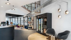 A modern interior with a reception desk, seating area, and a staircase leading to an upper level. - Campanile Katowice (Katowice)