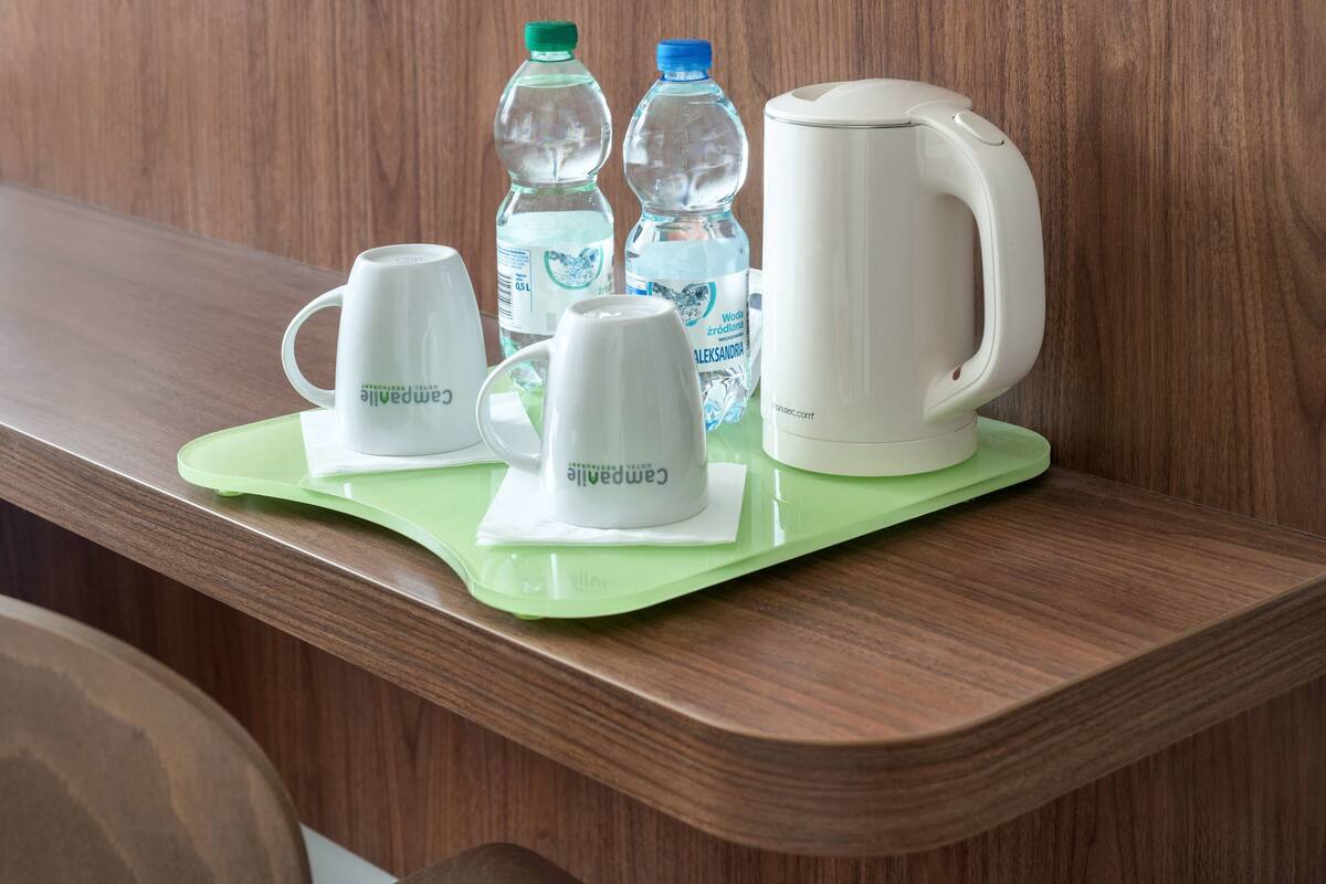 A wooden counter with a green tray holding two white mugs, two water bottles, and a white electric kettle.