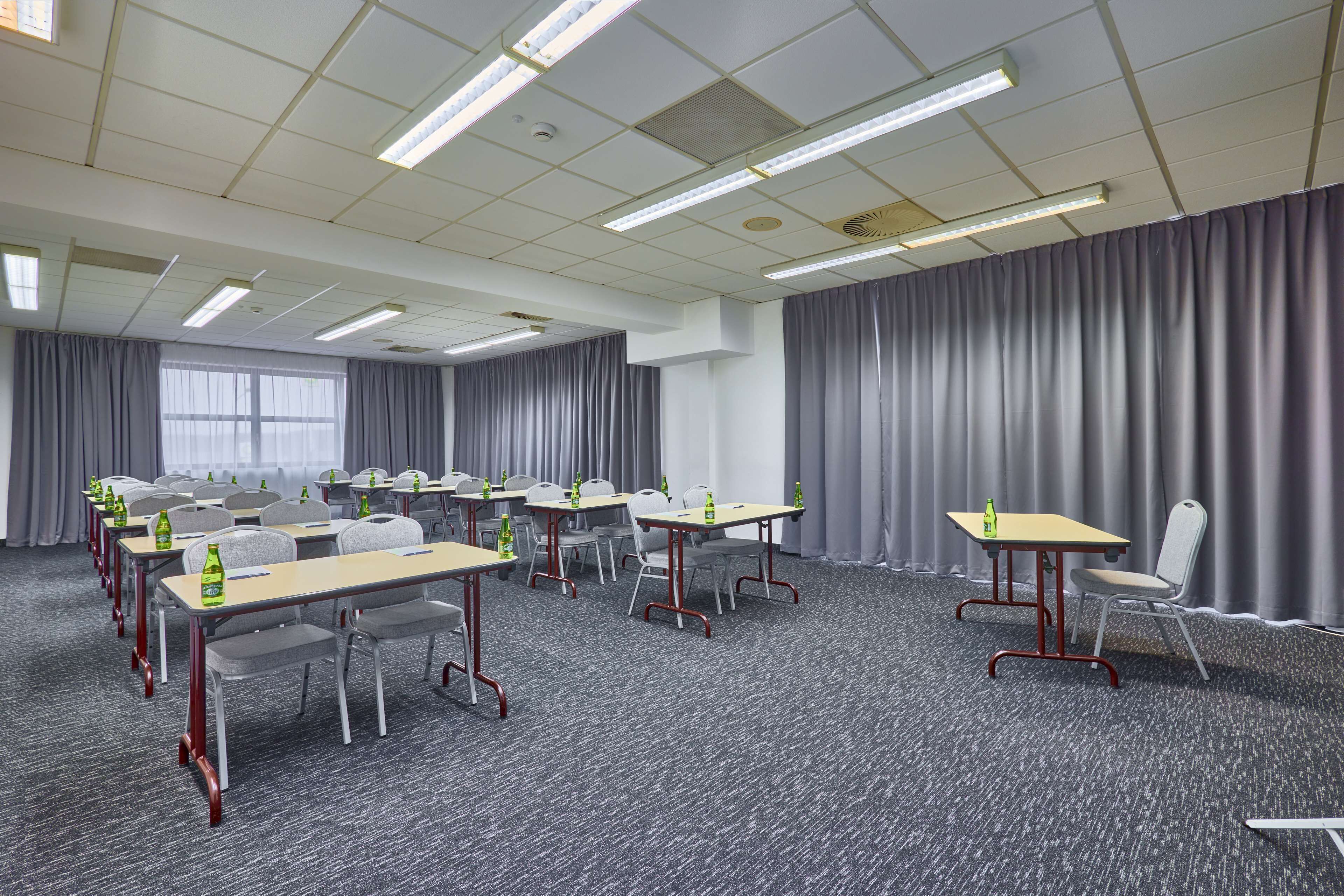 A conference room with multiple tables and chairs, equipped with water bottles, arranged in rows.