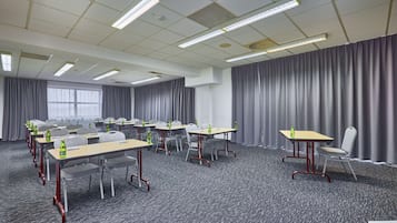 Un salón de conferencias con varias mesas y sillas, equipado con botellas de agua, dispuesto en filas.