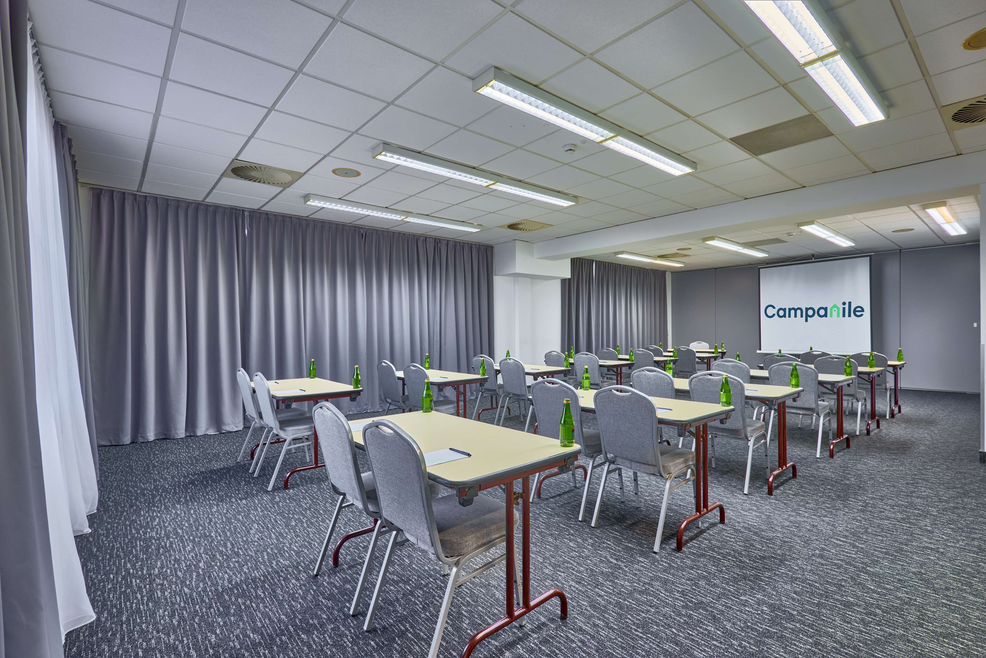 Un salón de conferencias con mesas, sillas y una pantalla de proyector mostrando 'Campanile'.