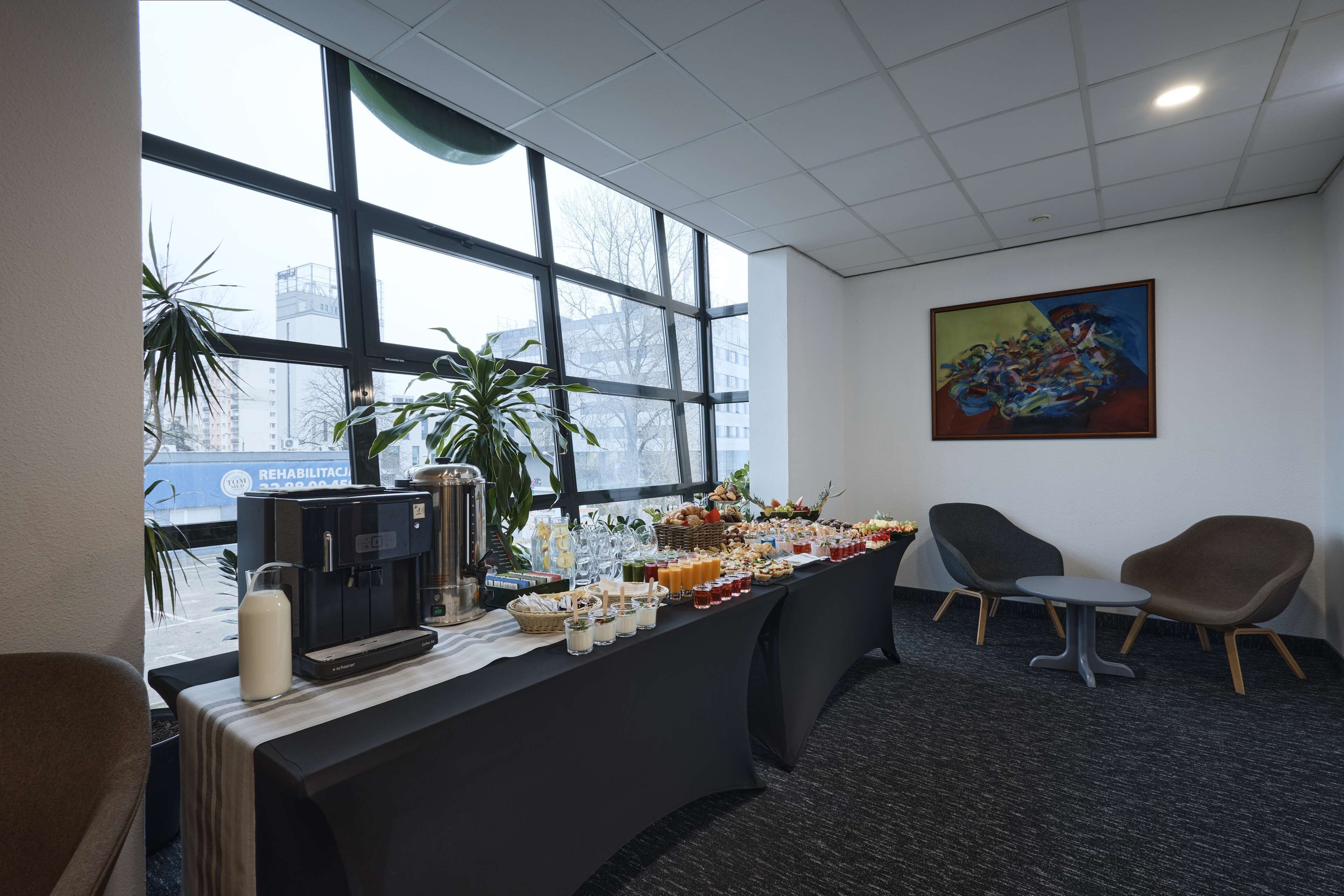 Una zona de recepción con una mesa de buffet, sillas, una máquina de café y un cuadro en la pared.