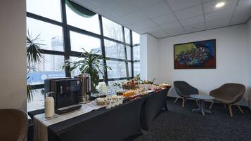 Una zona de recepción con una mesa de buffet, sillas, una máquina de café y un cuadro en la pared.