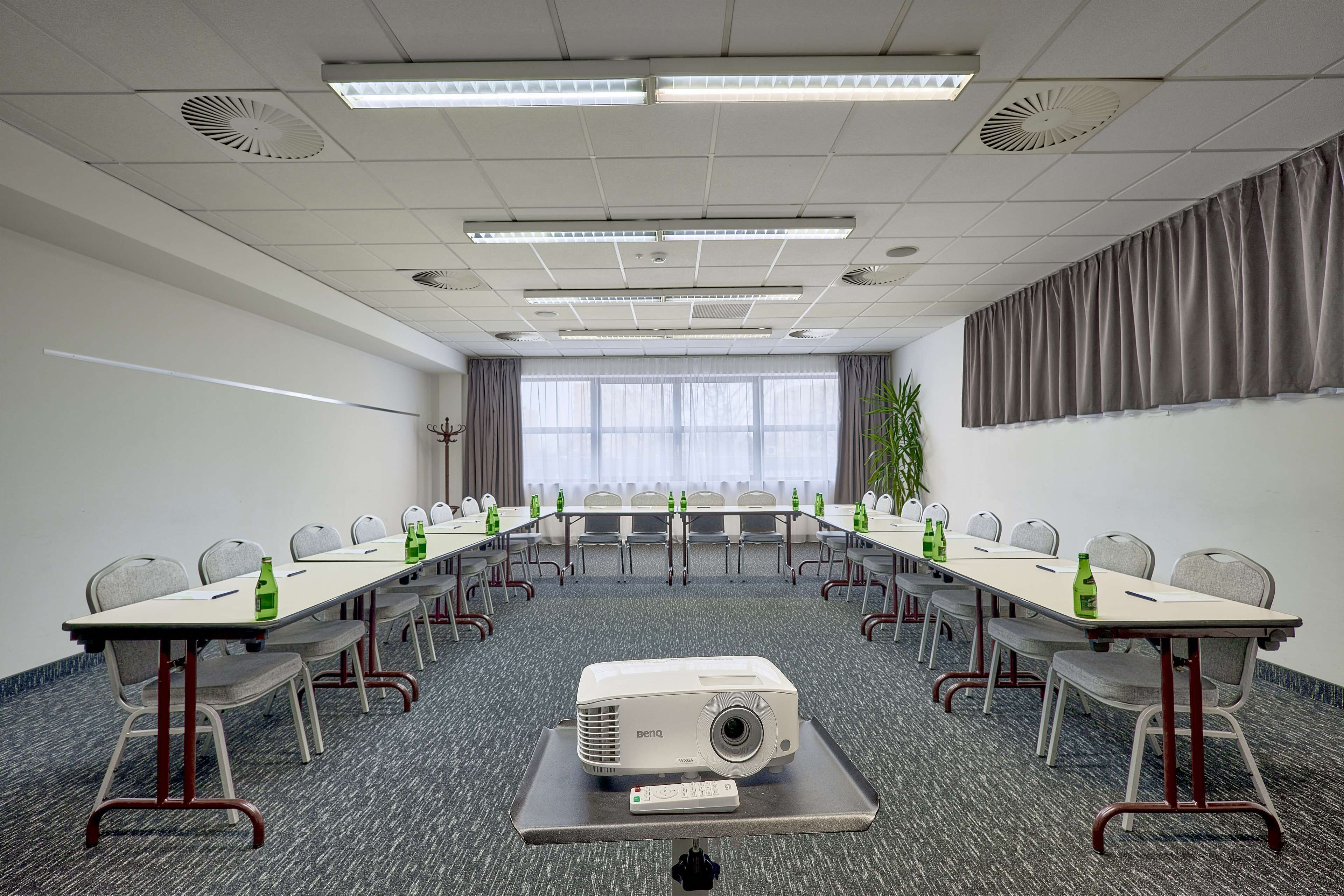 Una sala de conferències amb una taula llarga, cadires, un projecte i un comandament a distància.