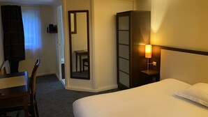 A hotel room with a bed, a desk, a chair, a wardrobe, and a mirror. - Hôtel Inn Design Le Havre Nord Montivilliers (Montivilliers)