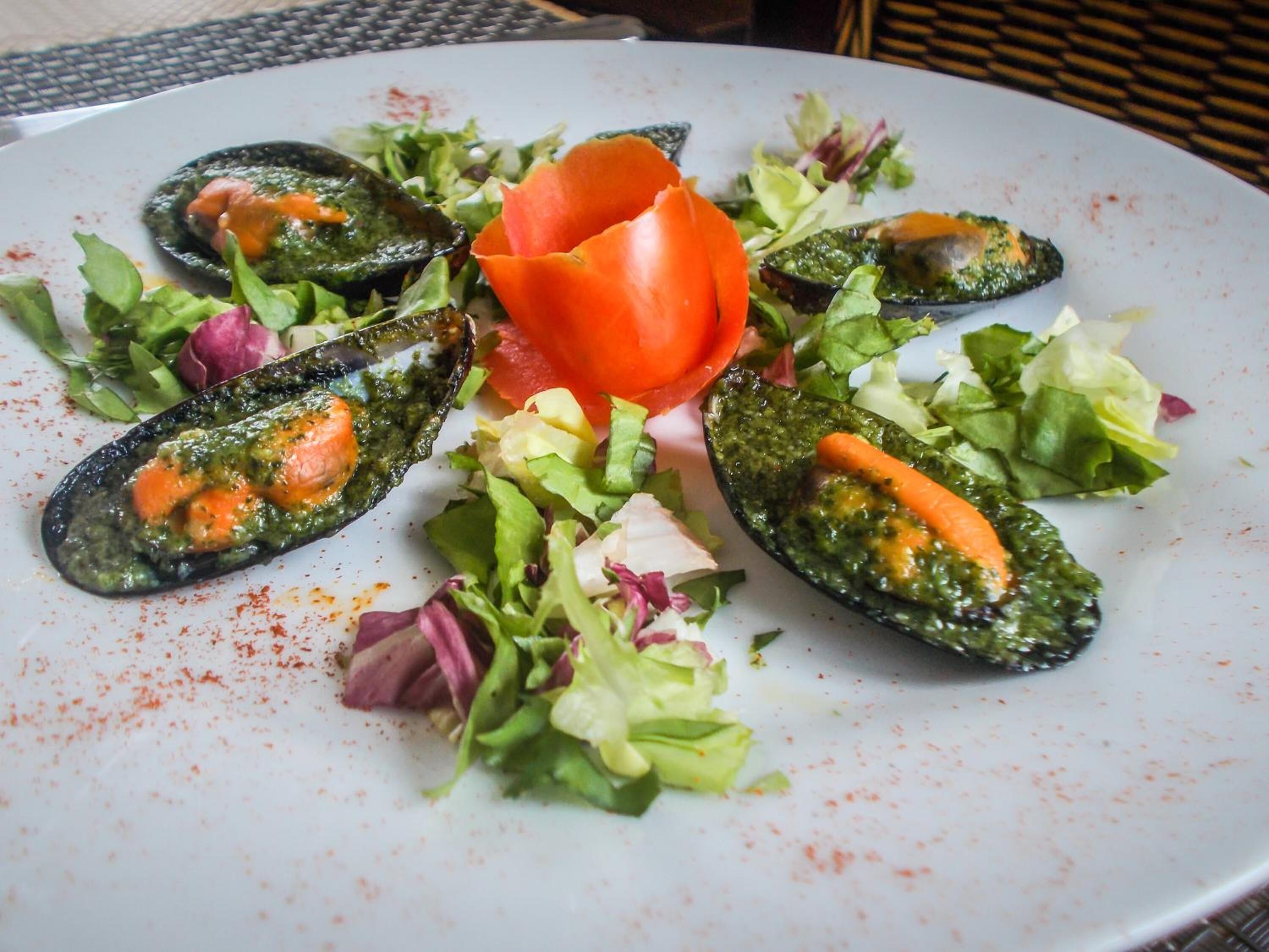 Een bord met mosselen, gegarneerd met tomaat en salade.