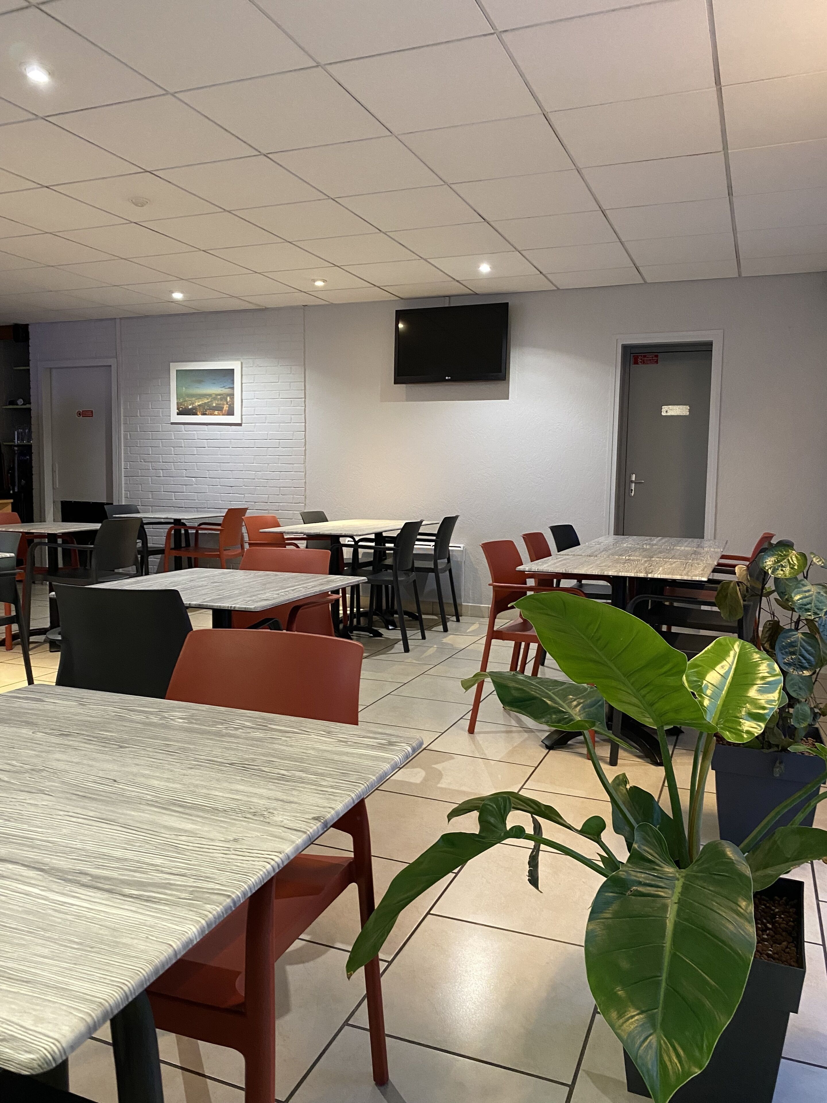 A modern dining area with multiple tables and chairs, a flat-screen TV mounted on the wall, and a door with a sign.