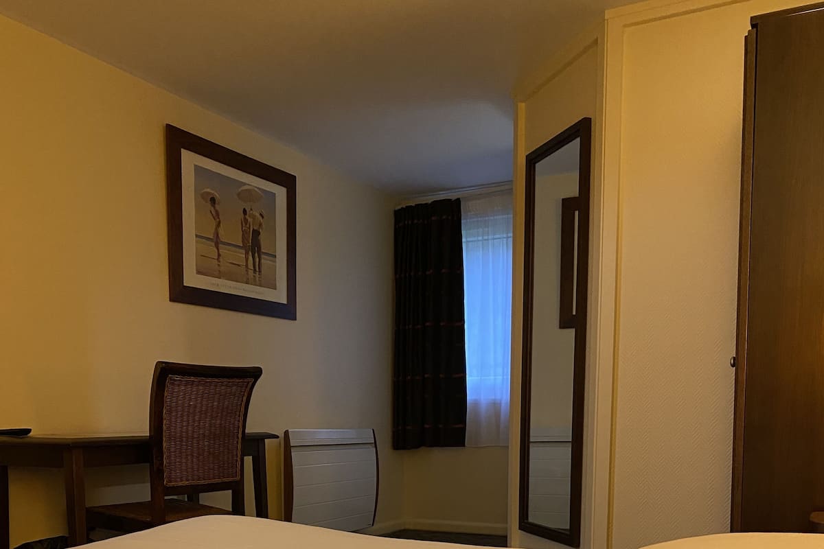 Ein Hotelzimmer mit einem Bett, zwei Stühlen, einem Schreibtisch, einem gerahmten Bild an der Wand und einer Tür.