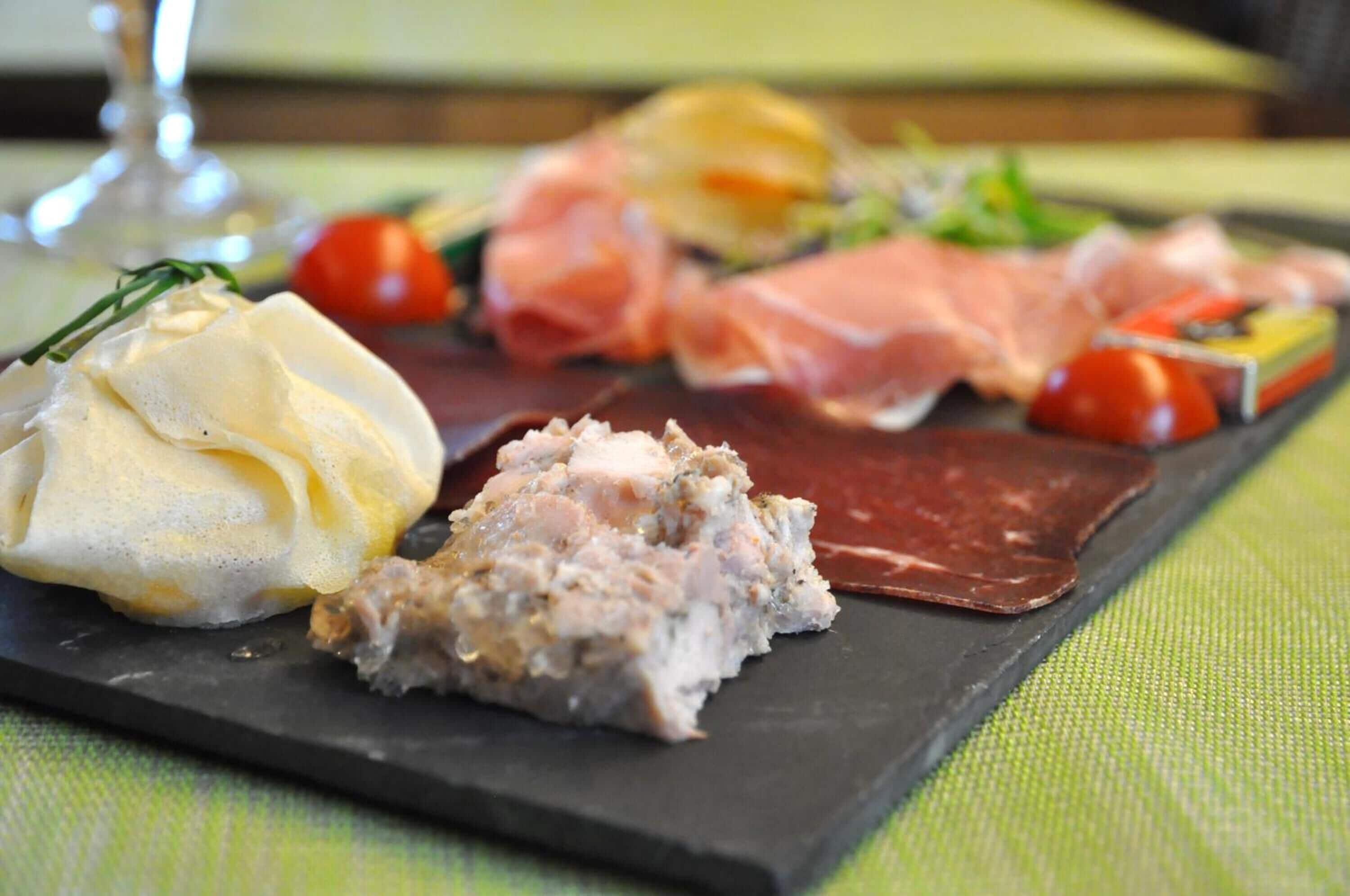A charcuterie board with various meats, cheese, and a small dish of pâté.