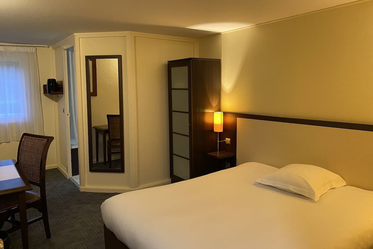 Ein Hotelzimmer mit Bett, Schreibtisch, Stuhl, Spiegel und Nachttisch mit Lampe.