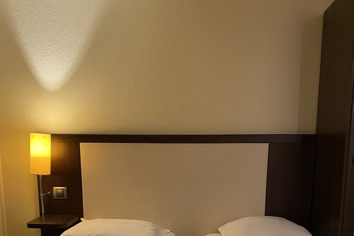 Ein Hotelzimmer mit zwei Einzelbetten, einem Nachttisch mit Lampe und einer Wandleuchte.
