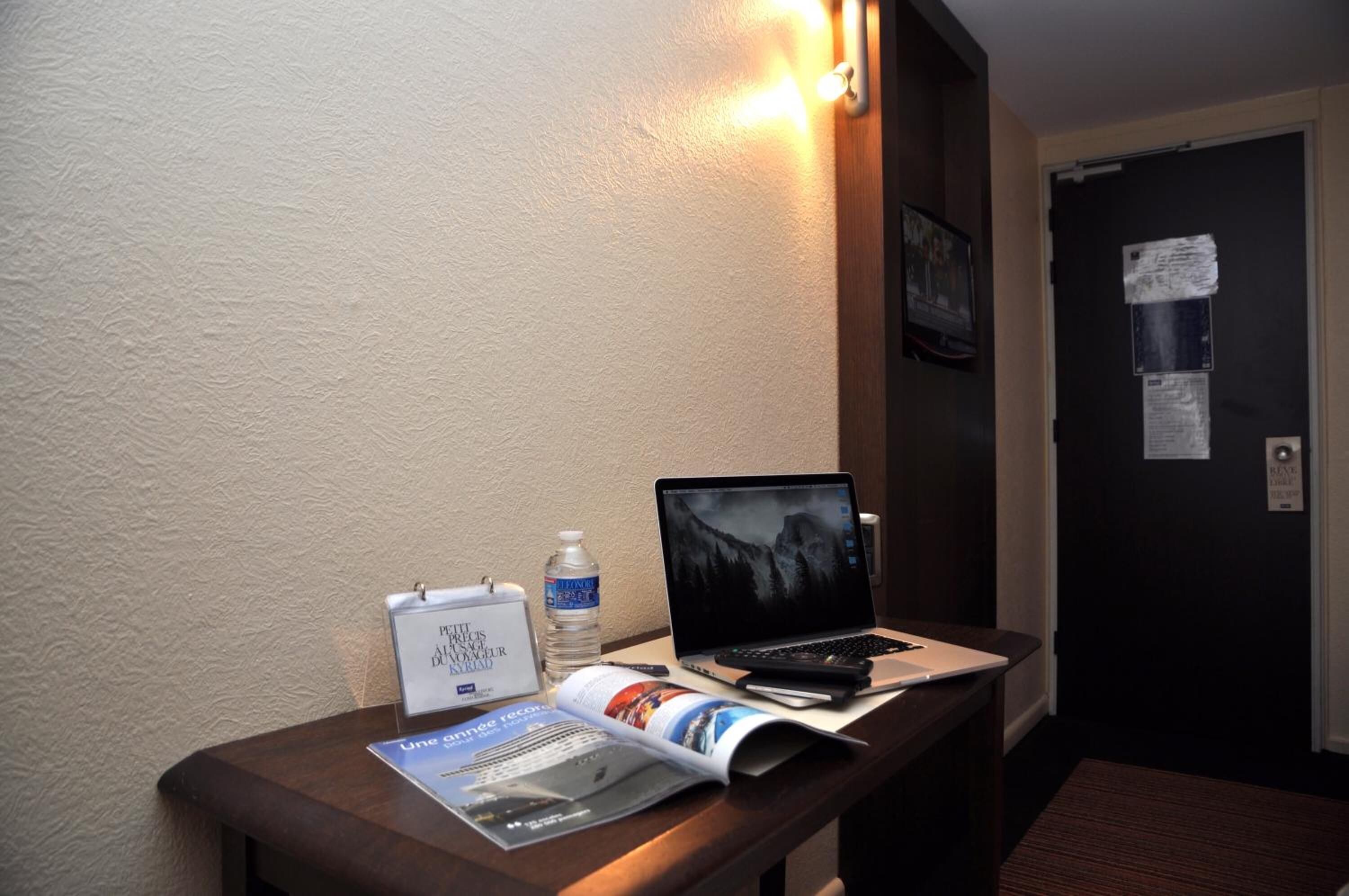 A hotel reception desk with a laptop, a water bottle, a name card holder, and a magazine.