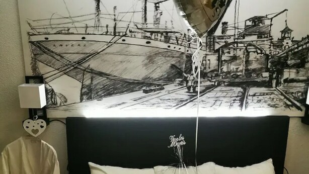 A hotel room with a bed featuring a 'Just Married' heart decoration, a wall mural of a ship, and a heart-shaped balloon tied to the bed. - Hôtel Kyriad Lille Nord - Roncq (Roncq)