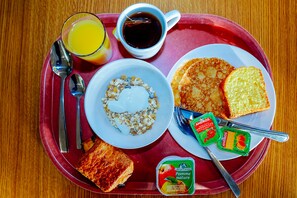 Een ontbijfwagen met toast, pannenkoeken, een kom cornflakes met yoghurt, een glas sinaasappelsap, een kop koffie en twee yoghurtbekers.