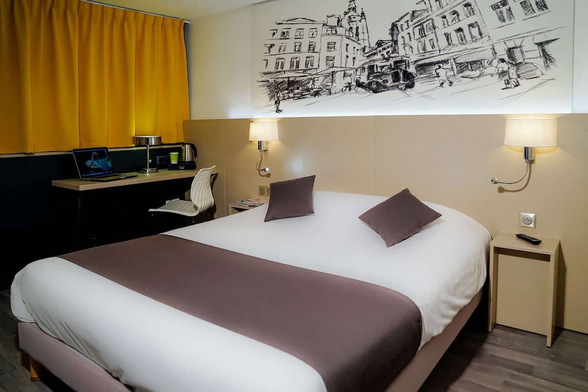 Een hotelkamer met een groot bed, een bureau met een laptop, een lamp en een kunstwerk aan de muur.