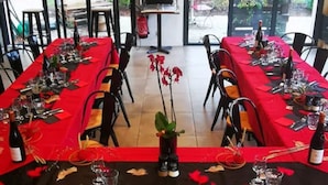 A large dining area with red tablecloths and black chairs, featuring a central floral arrangement and a dartboard on the wall. - Hôtel Kyriad Lille Nord - Roncq (Roncq)