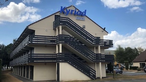 Um hotel chamado 'Kyriad', com design moderno, destacando uma escadaria imponente e várias varandas.