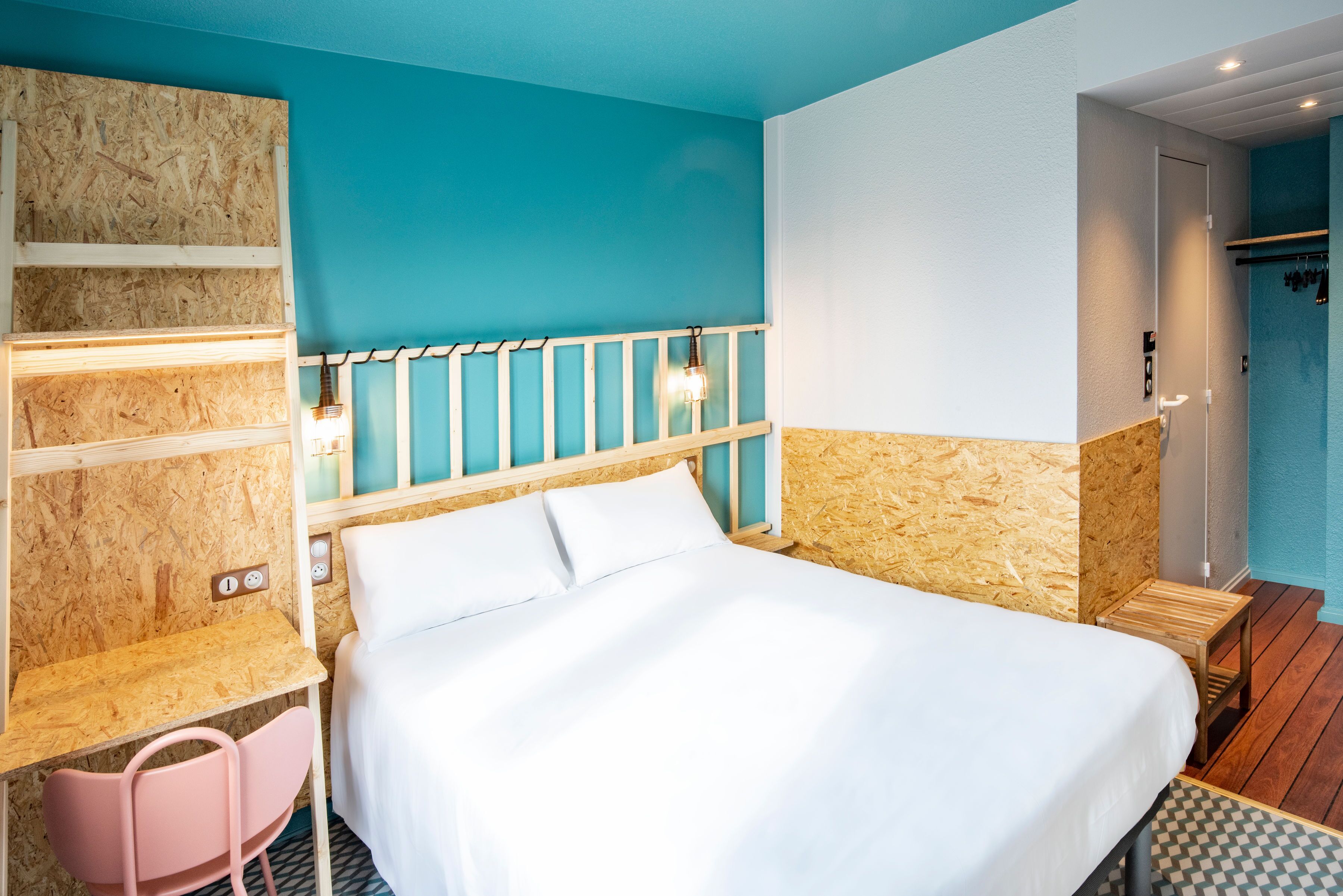 Una camera da letto con un letto, una scrivania in legno, una sedia rosa e uno sgabello.