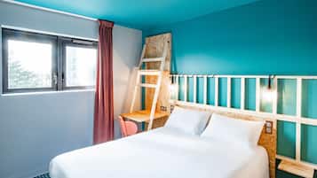 Ein Hotelzimmer mit Bett, Schreibtisch, Stuhl, einem Fenster mit Vorhängen und Blick ins Freie.