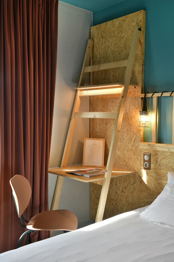 Una habitación con una cama, una escalera de madera, una silla y un estante en la pared con una lámpara.