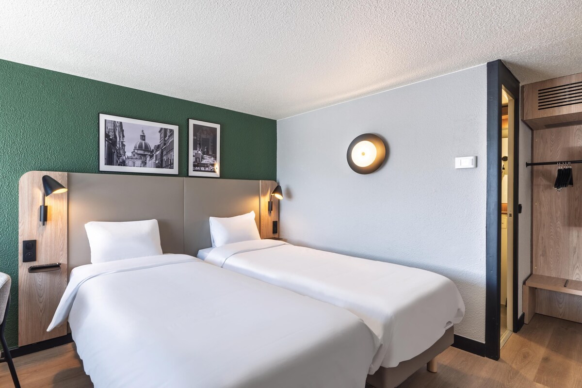 A hotel room with two beds, a desk with a chair, and a wardrobe.