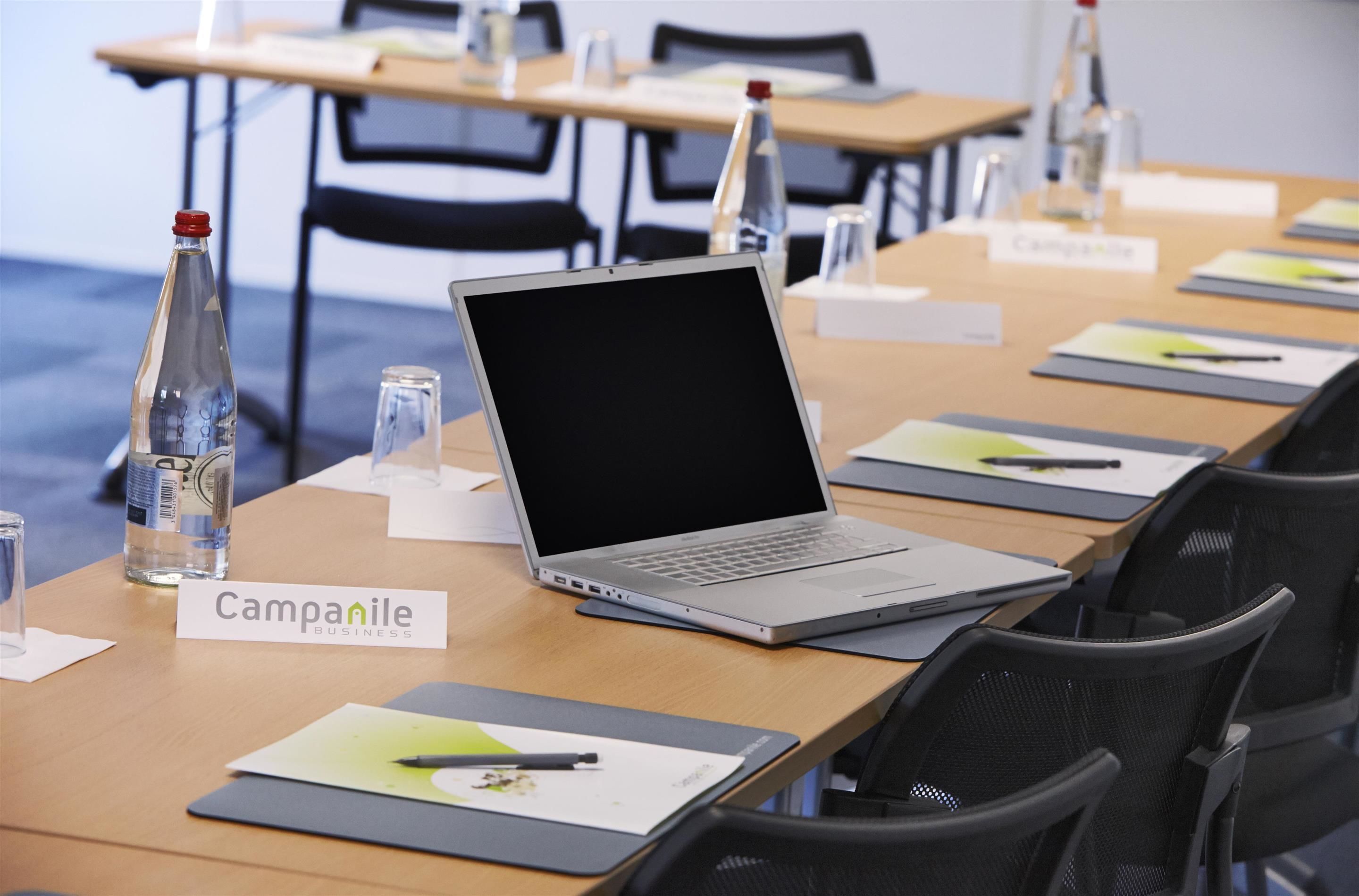 Una sala de conferencias con una mesa equipada con portátiles, tarjetas de identificación y botellas de agua.