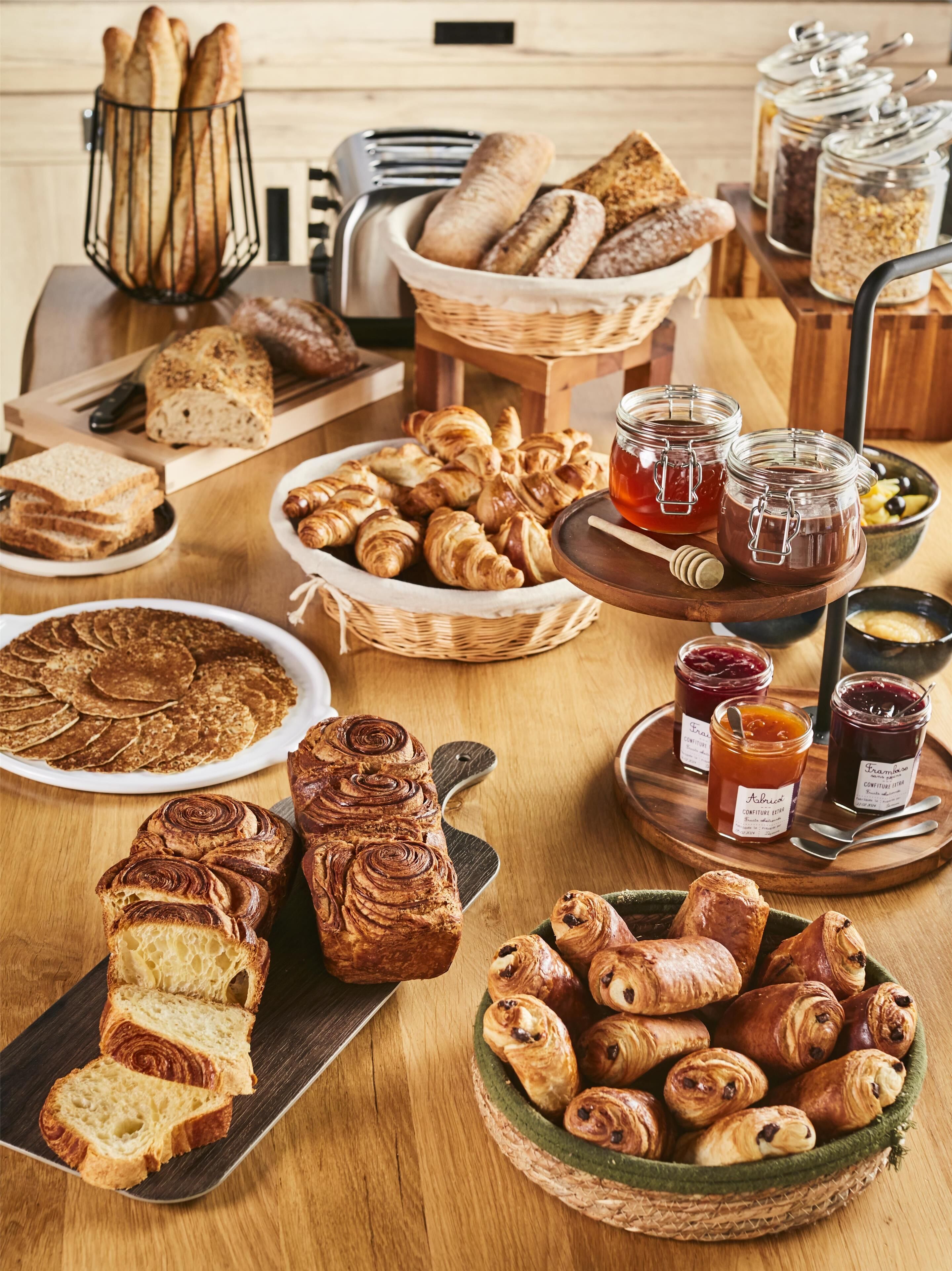 A variety of breads and pastries on a wooden table, including croissants, baguettes, and a loaf of bread.