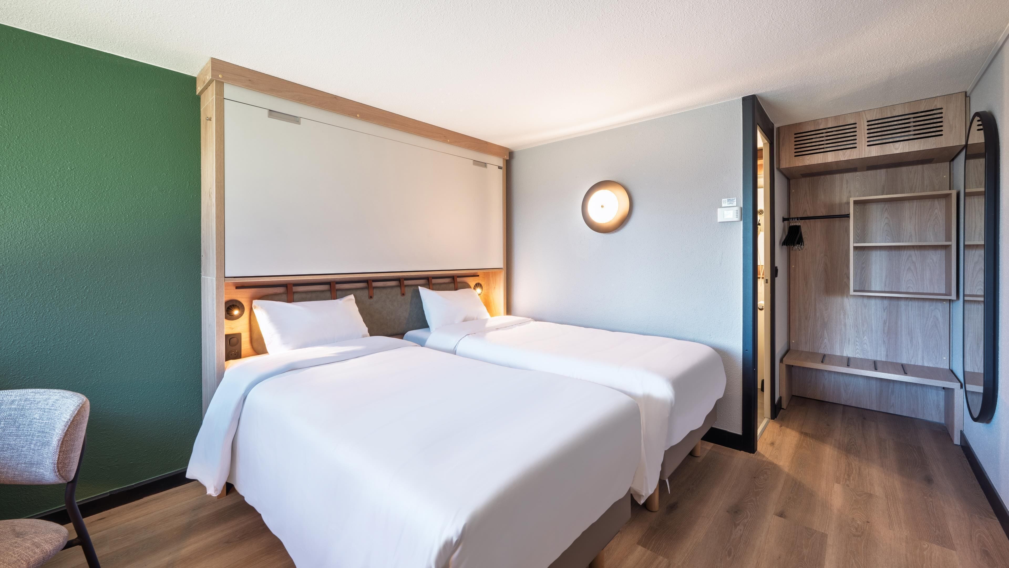 A hotel room with two beds, a wooden headboard, a wall-mounted light, and a built-in wardrobe.