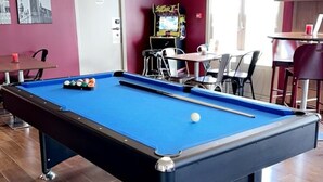 Una mesa de billar con superficie de fieltro azul, rodeada de suelo de madera.