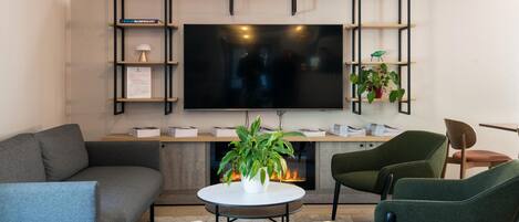 A modern living room with a sofa, chairs, a coffee table, a fireplace, a TV, and shelves with books and a plant.