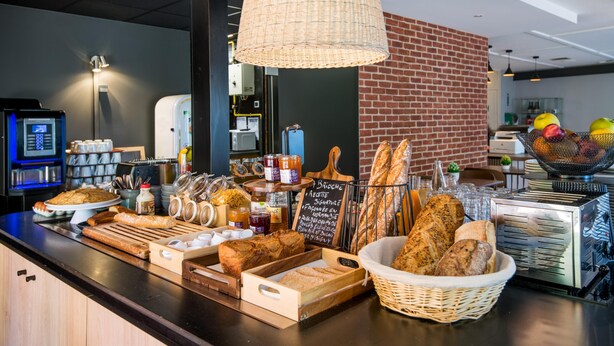 Mostrador de panadería con diversos panes, frascos de mermeladas y una cesta de frutas.