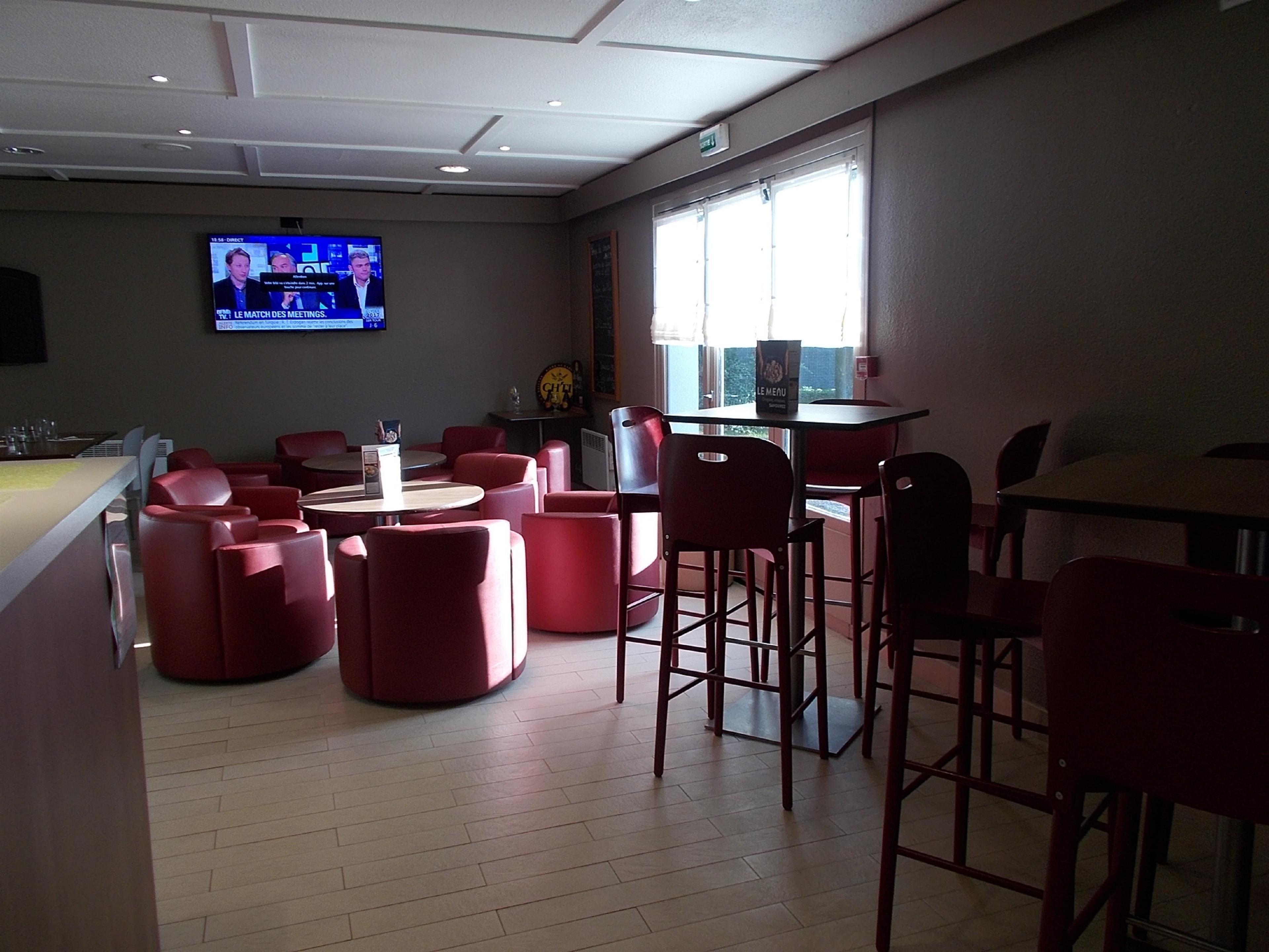 A modern restaurant with red seating, a TV displaying news, and a window with natural light.