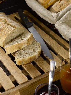 Des tranches de pain sur une planche à découper en bois, avec un couteau et un pot de confiture à côté.