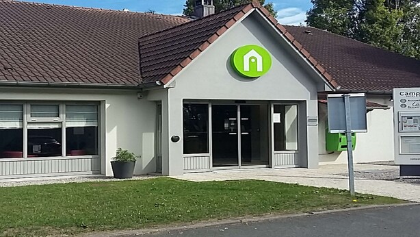 Ein modernes Gebäude mit grünem Logo, großen Fenstern und einem kleinen Garten.