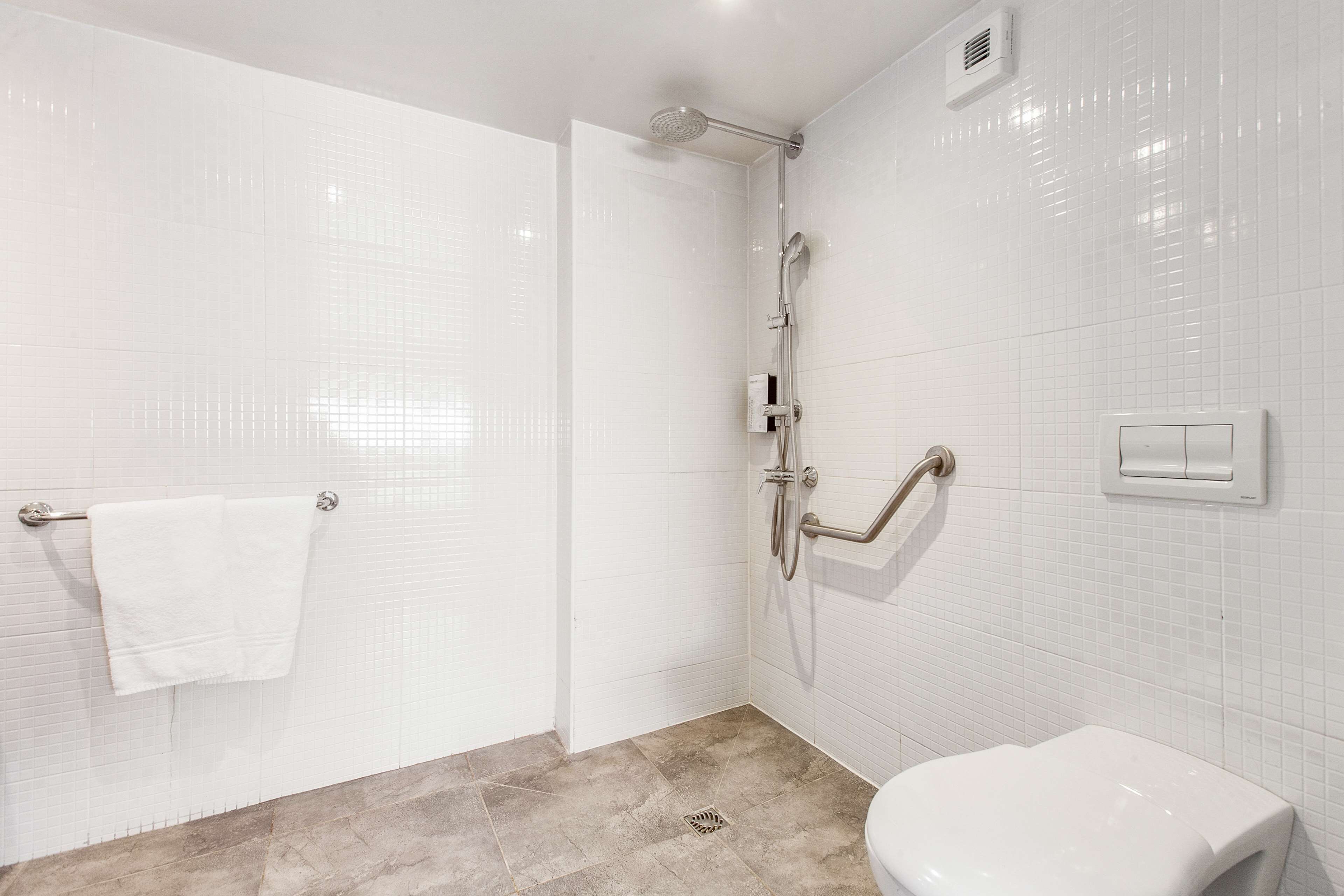 A modern bathroom with white tiled walls, a shower area, a toilet, and a towel rack.