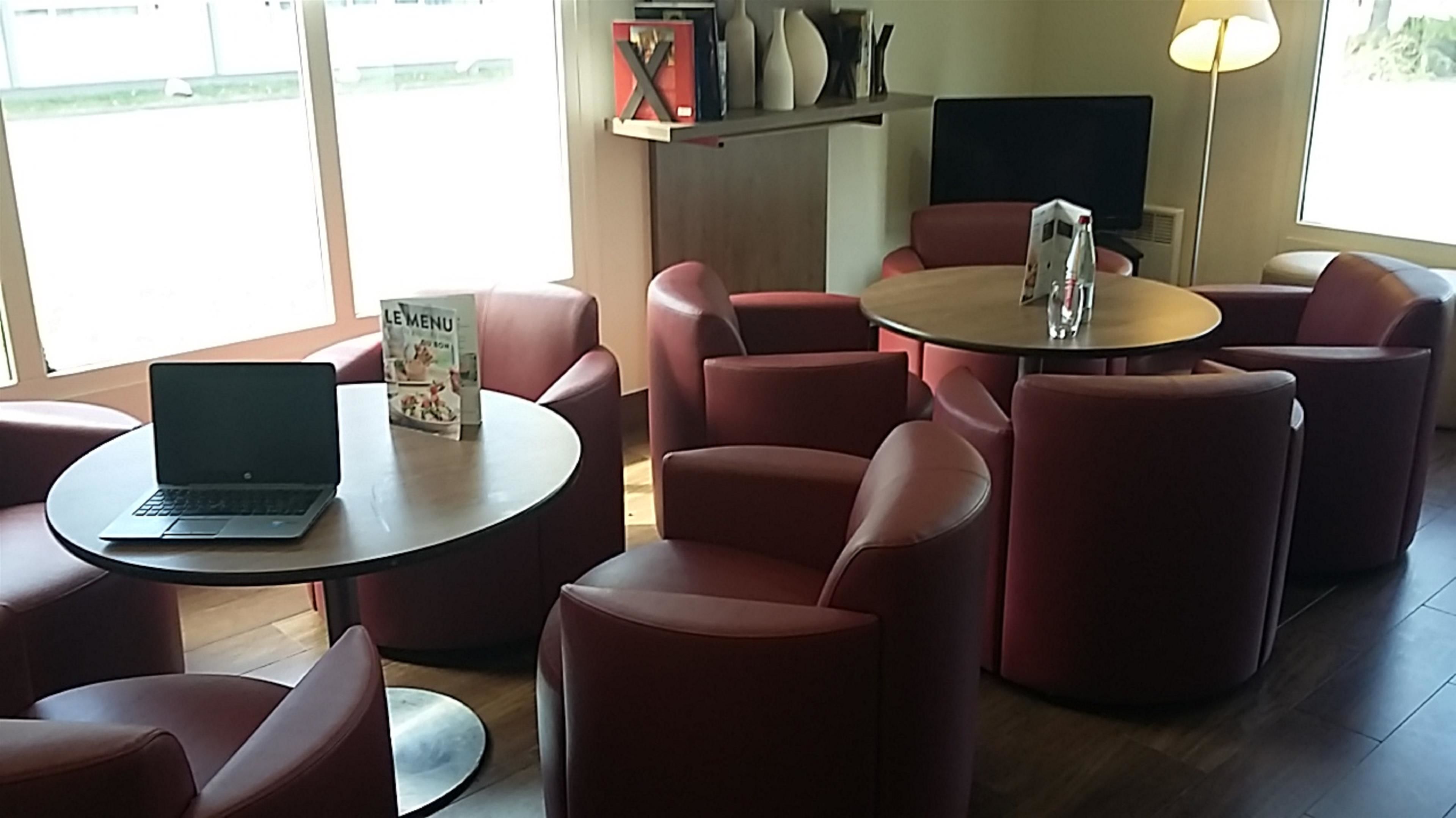 A seating area with round tables and cushioned chairs, a laptop on one table, and a menu stand.