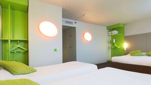 Ein Hotelzimmer mit zwei Betten, grünen Kissen, einem Kleiderschrank und einem Spiegel.