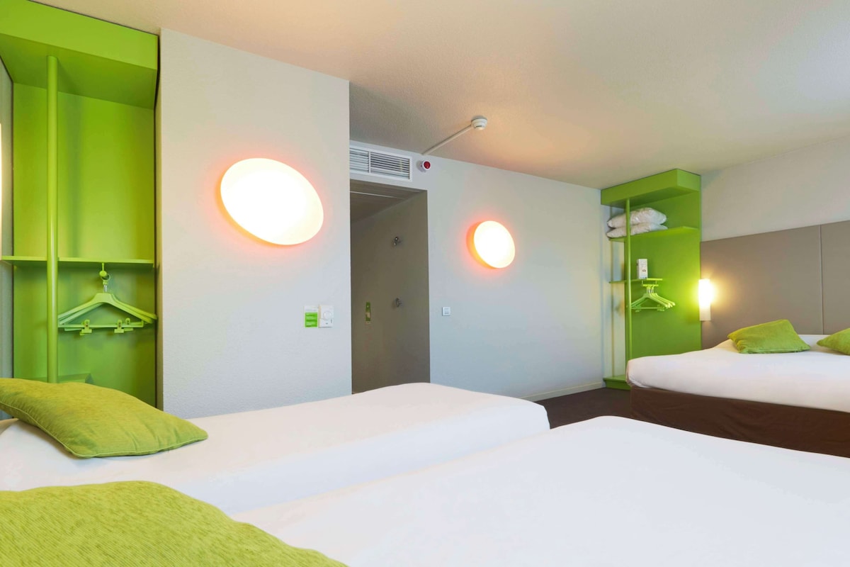 Habitación de hotel con dos camas, almohadas verdes, un armario y un espejo.