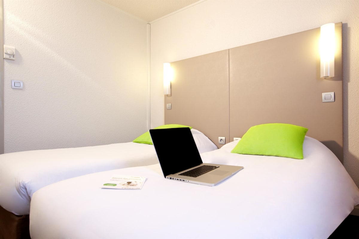 Une chambre d’hôtel avec deux lits, un ordinateur portable sur le lit de gauche et une brochure sur le lit.