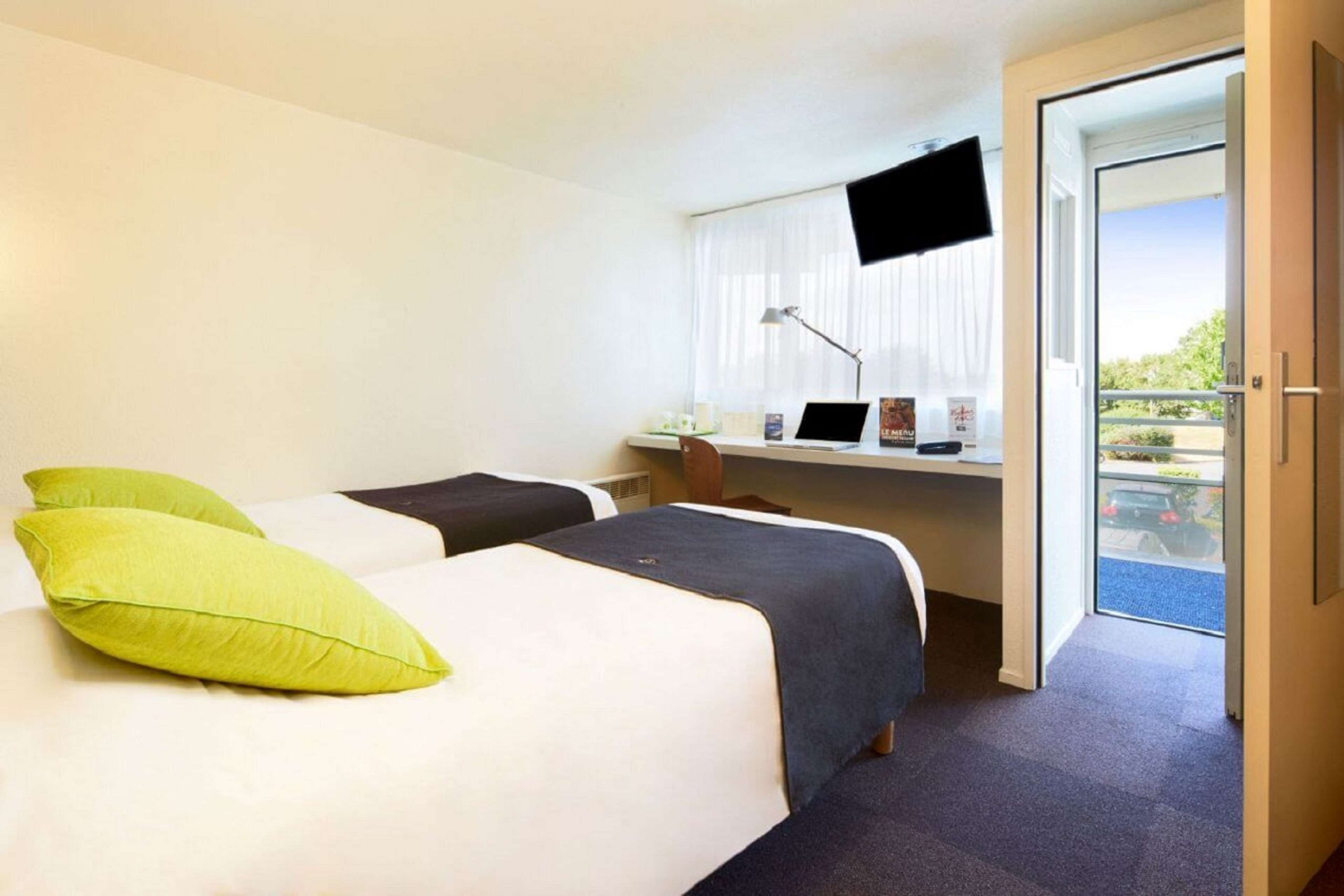 Habitación de hotel con dos camas, un escritorio con una computadora portátil, un televisor y un balcón con vistas.