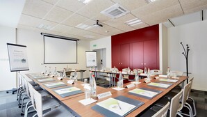 Ein Konferenzraum mit einem langen Tisch, Stühlen, Namensschildern, Wasserflaschen und Präsentationsbildschirmen.